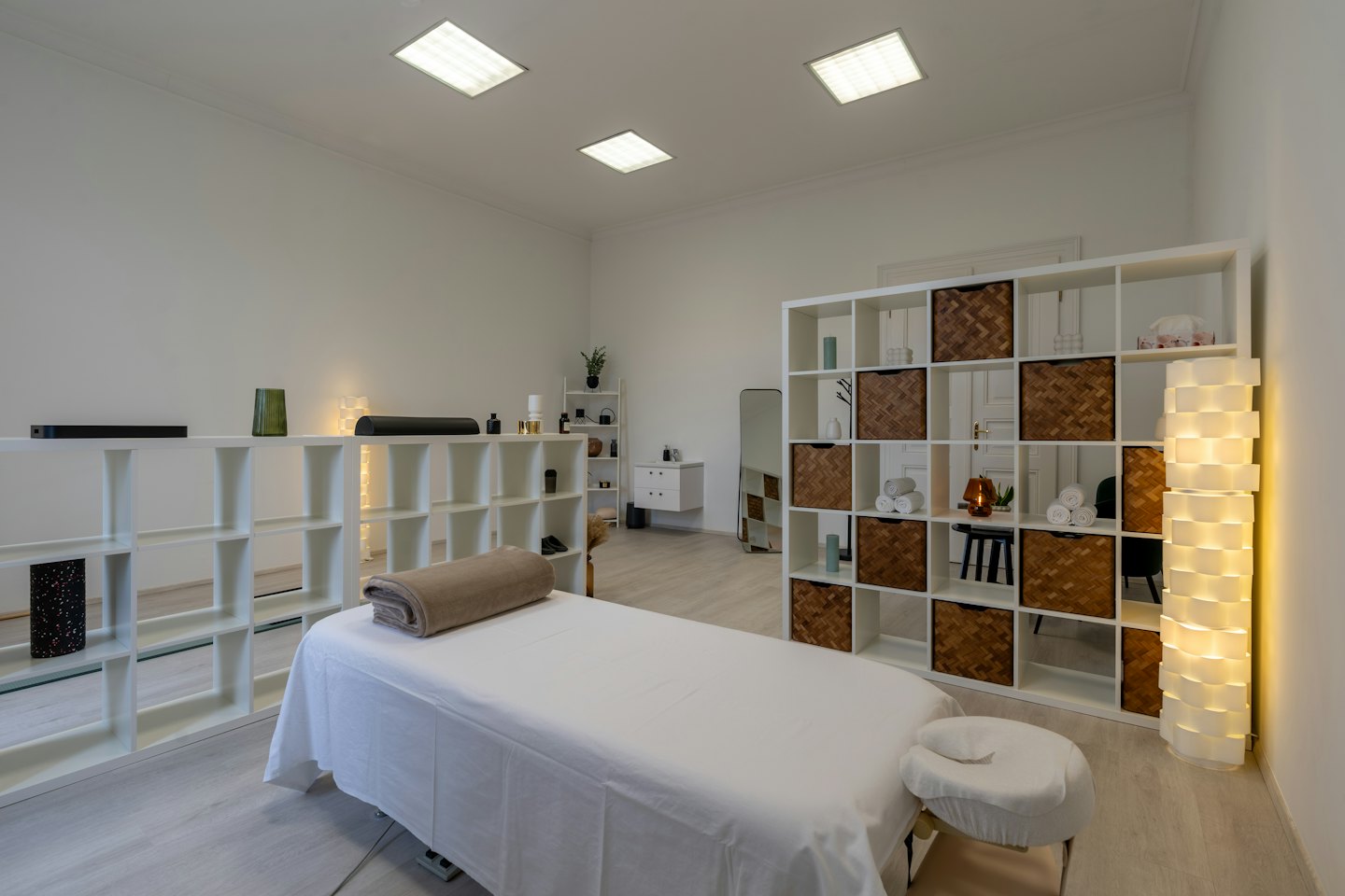 Stanza moderna e luminosa per terapie con lettino da massaggio bianco e scaffalature.